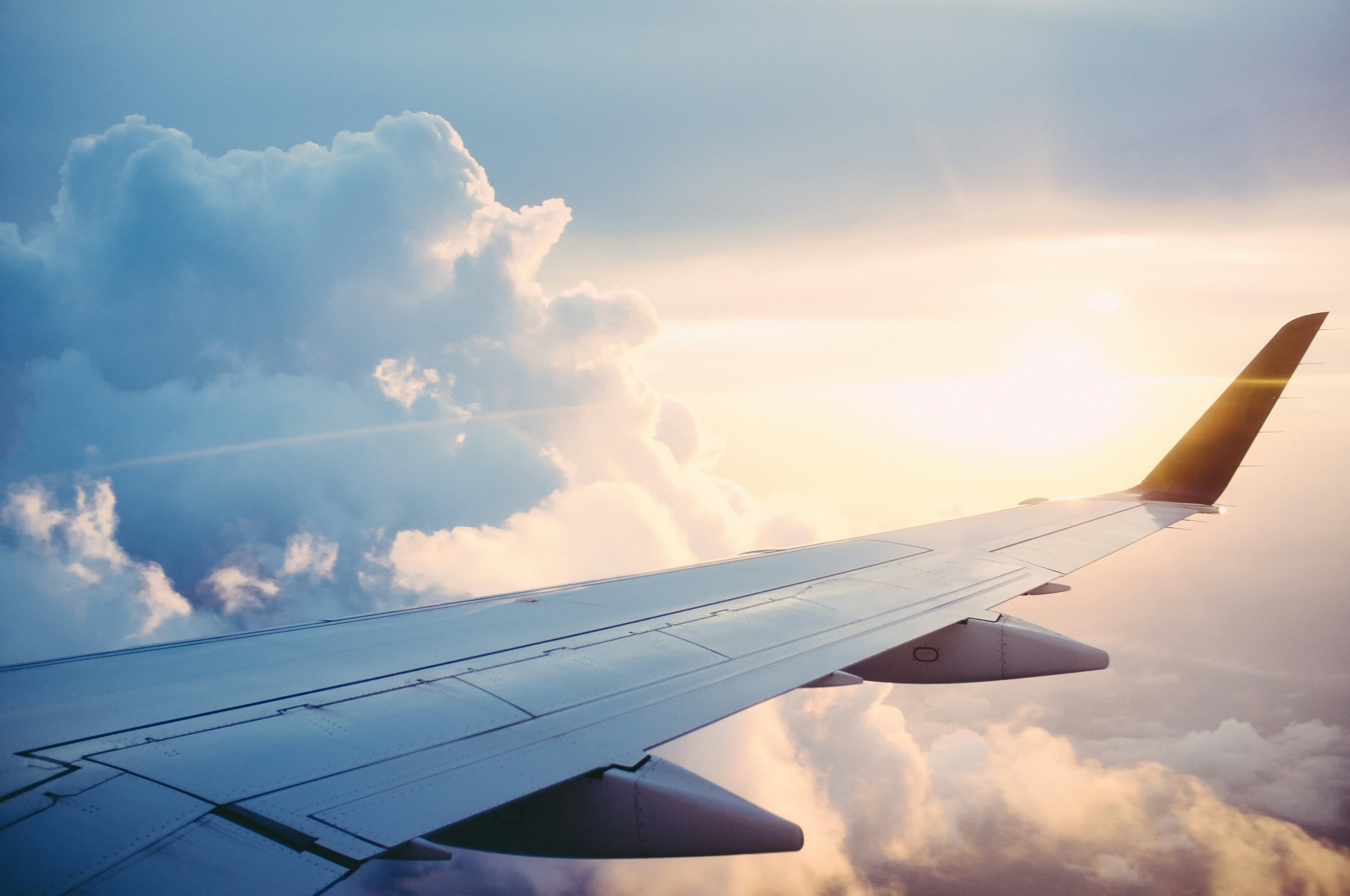 Aircraft wing over clouds at sunset, photographed from a passenger window