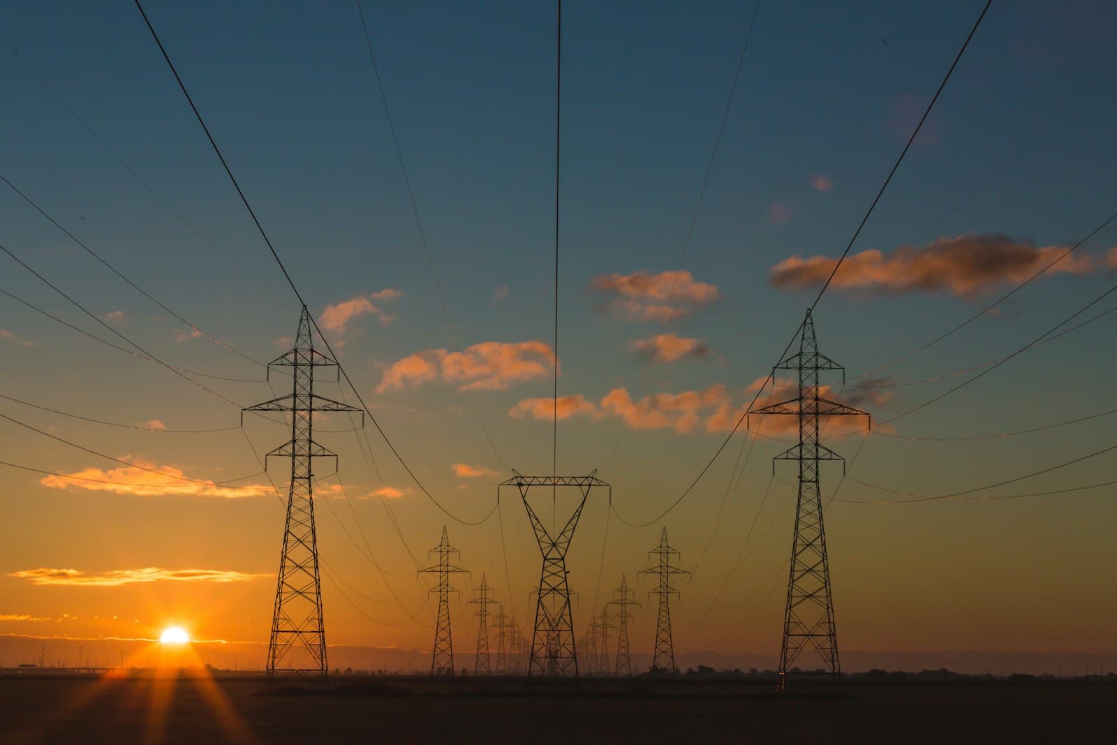 High-voltage transmission towers and power lines silhouetted at sunset