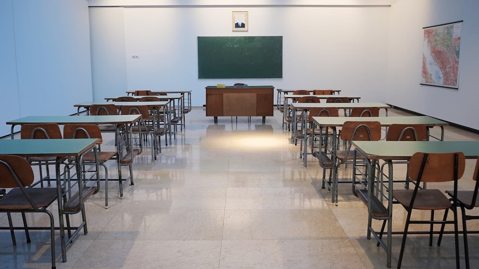 Empty school classroom with rows of desks facing a green chalkboard