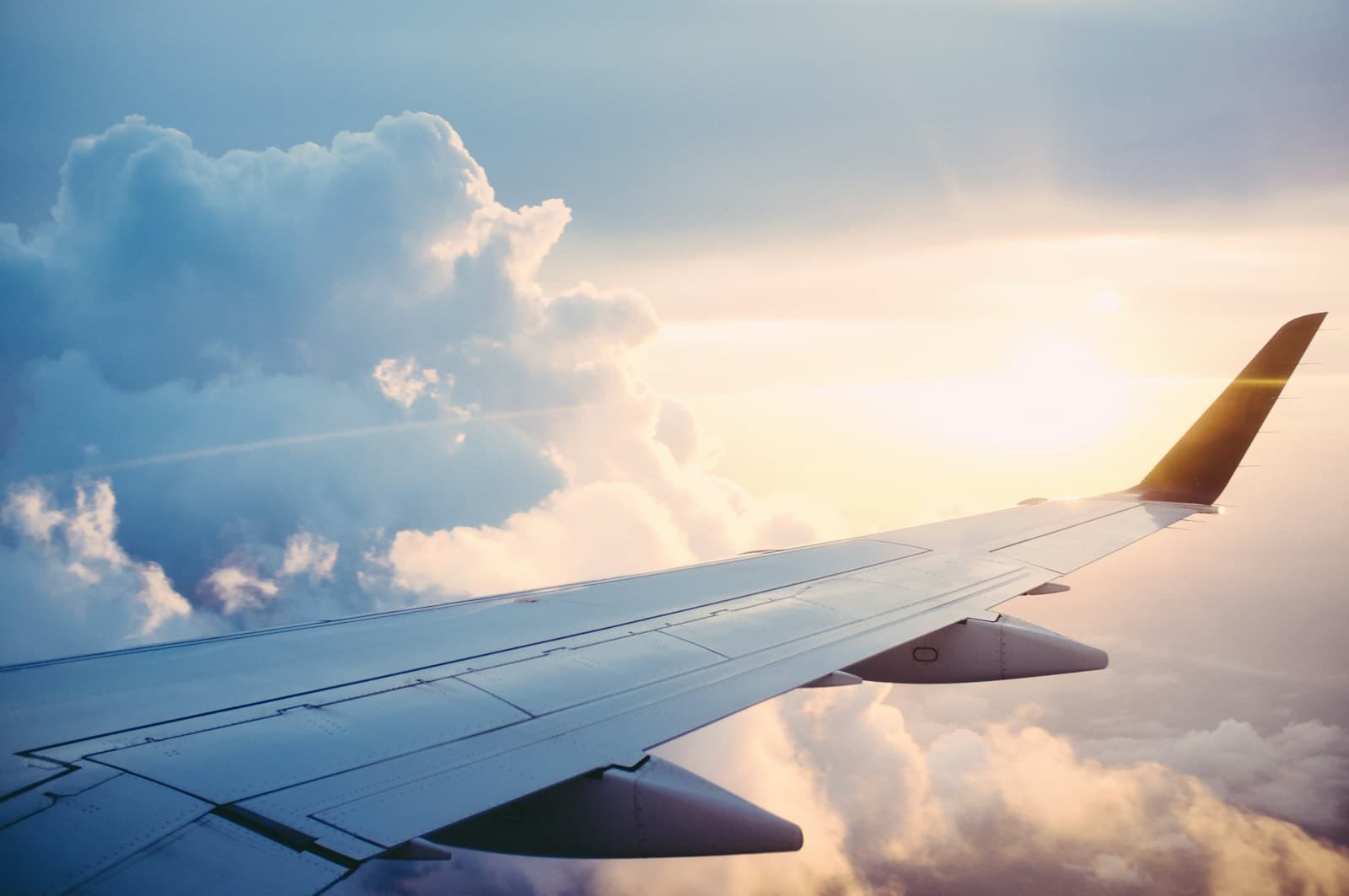 Passenger jet wing in flight above clouds at sunset, showing the lower wing surface and engine