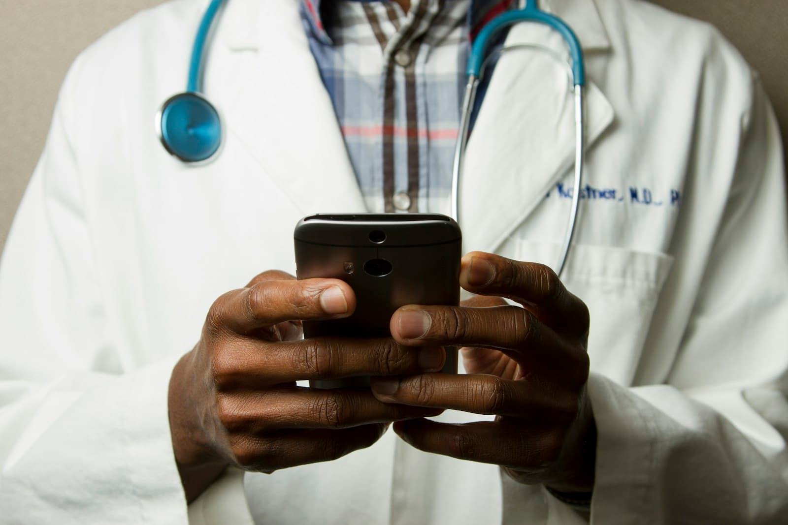 Physician in a white coat with a stethoscope holding a mobile phone